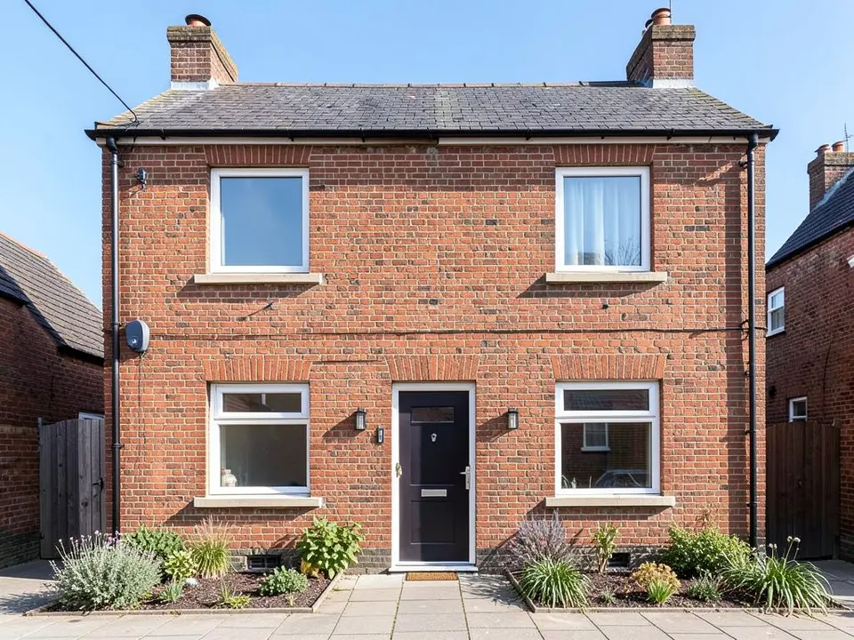 Front of a red brick two-storey house with chimneys, a dark front door, two ground-floor windows and two plain flat upstairs windows