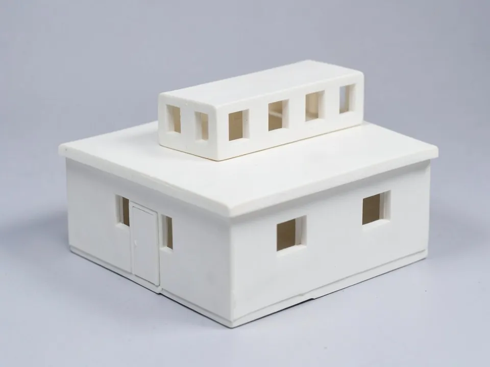 A white clay model of a single-storey house with a flat roof and a raised long box on top with a row of window openings