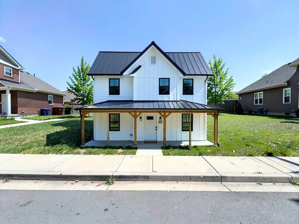 The same lot with a new two-storey white board-and-batten farmhouse with a black metal gable roof, black windows, a covered front porch on wood posts and a short path to the sidewalk; neighbours, sidewalk and street unchanged