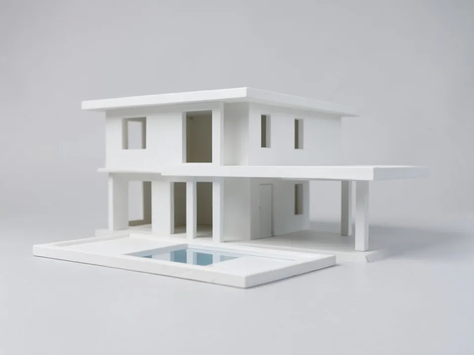 A plain white clay model of a two-storey flat-roofed house with a side canopy on posts and a pool, on a light grey ground