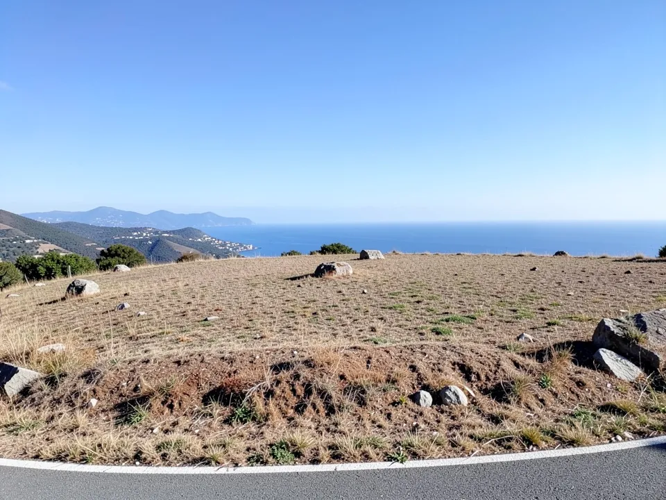 An empty dry-grass hillside with rocks, a view over the sea and hills and a curving road