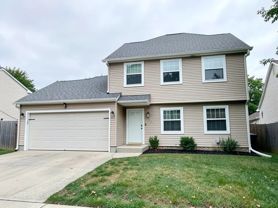 Front of a two-storey house with beige horizontal siding, a grey shingle roof, white-framed windows, a double garage on the left, a plain white front door, a lawn and a concrete driveway under an overcast sky