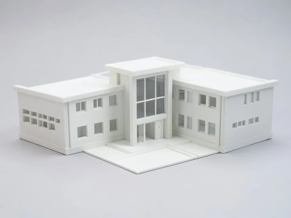 A plain white clay model of a school with two two-storey wings meeting at a tall glazed entrance hall, flat roofs and a forecourt