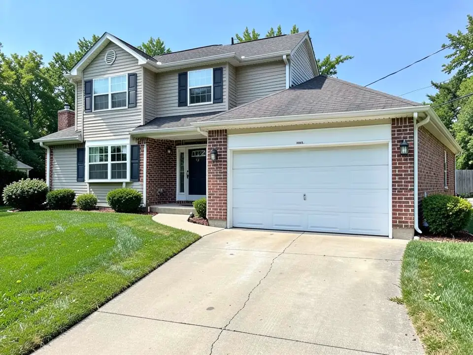 Front of a two-storey beige-sided house with brick trim and an attached garage with one white roll-up door, a concrete driveway with a crack, and a lawn
