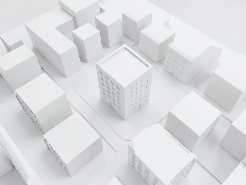 All-white massing model seen from above at an angle: a city block of plain white boxes of different heights along two streets with one slightly taller box with window rows in the middle, on flat white ground with no trees